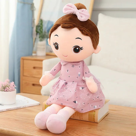 Plush toy doll with brown hair and a pink dress sitting on a wooden surface.