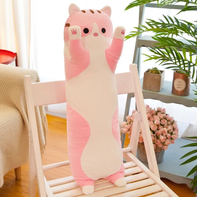 Large pink and beige cat-shaped plush toy on a wooden chair with a home interior background.