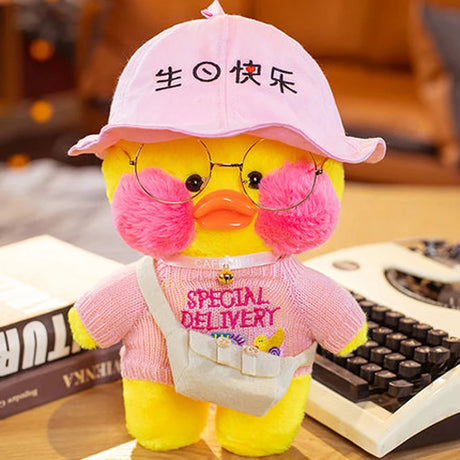 Plush toy duck wearing a pink cap and sweater with glasses, sitting on a desk.
