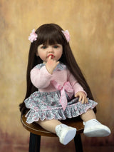 Doll with long dark hair and pink bows, wearing a pink top and patterned skirtbrown background.