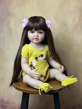 Doll with long brown hair wearing a yellow outfit on a wooden stool 