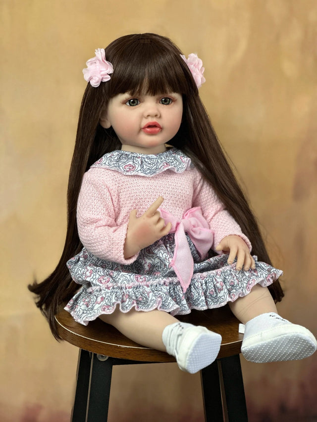 A doll with long dark hair and a pink outfit sitting on a wooden stool 