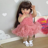 Doll in a pink dress with a tiara, standing against a decorative wall with hearts and a birthday card.