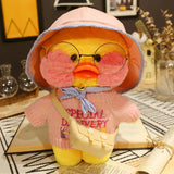 Plush toy duck wearing glasses and a pink outfit with text, on a surface with decorative items in the background.