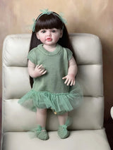 Child-like doll in a green dress sitting on a white chair.
