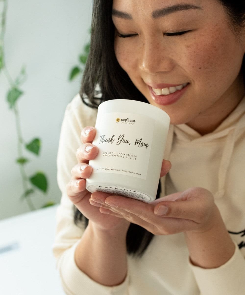 Woman holding a white candle with text, smiling in a casual setting