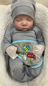 Newborn baby in a gray outfit with cartoon design, lying on a soft surface.