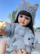 Child wearing a gray knitted outfit with cat ears and holding a matching cat plush toy outdoors.