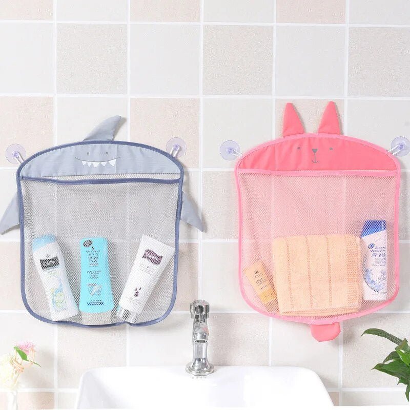 Two mesh storage bags, one shark-shaped and one pink bunny-shaped, hanging on a tiled wall with bath products inside.