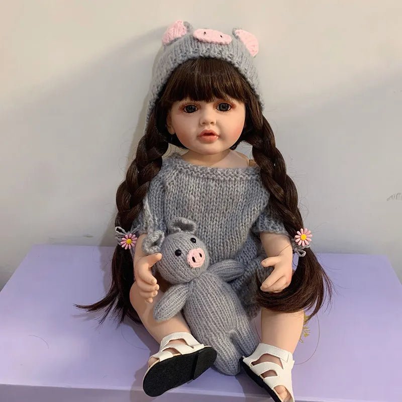 A doll wearing a knitted outfit with a pig-themed hat and holding a small pig plush toy
