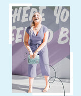 Woman in a purple outfit holding a turquoise clutch against a colorful background