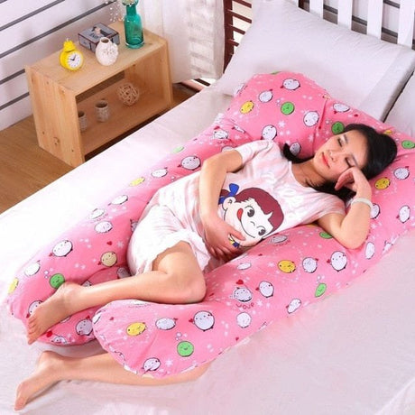Woman lying on a pink U-shaped pillow with cartoon patterns in a bedroom setting.