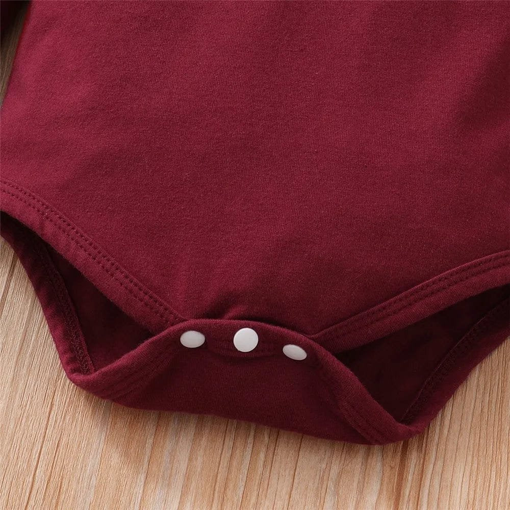 Close-up of a maroon baby romper with buttons on a wooden surface