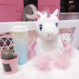 Plush unicorn toy with a gradient cup and small plant in a pink pot on a white surface.