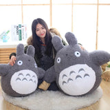 Person sitting with two large plush Totoro toys on a wooden floor.
