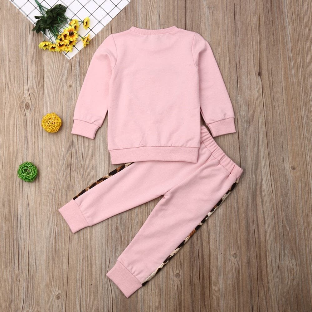 Pink children's sweatshirt and pants set on a wooden surface with decorative elements.