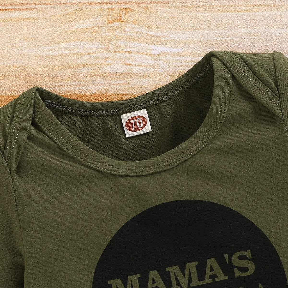 Green baby onesie with 'MAMA'S' text on a wooden surface