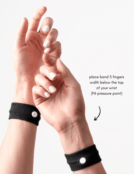 Hands wearing black wristbands with white buttons, demonstrating a pressure point.