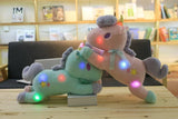Two plush toys, one green and one pink, with colorful lights on a wooden table.