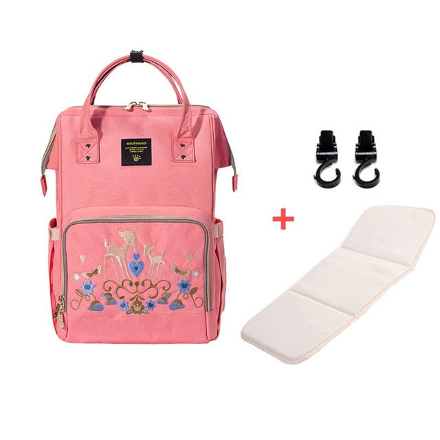Pink backpack with embroidery, white mat, and black hooks.