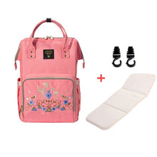Pink backpack with embroidery, white mat, and black hooks.