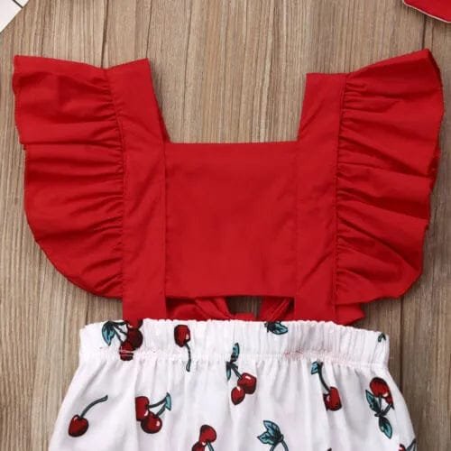 Red ruffled top and white shorts with cherry pattern on a wooden surface