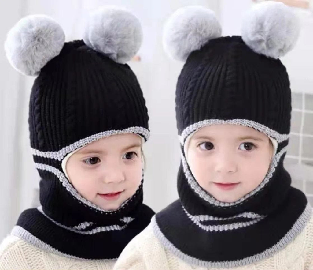Two children wearing black knit hats with white pom-poms and scarves on a plain background.