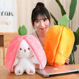 Person holding a plush strawberry and pineapple with a laptop on a desk
