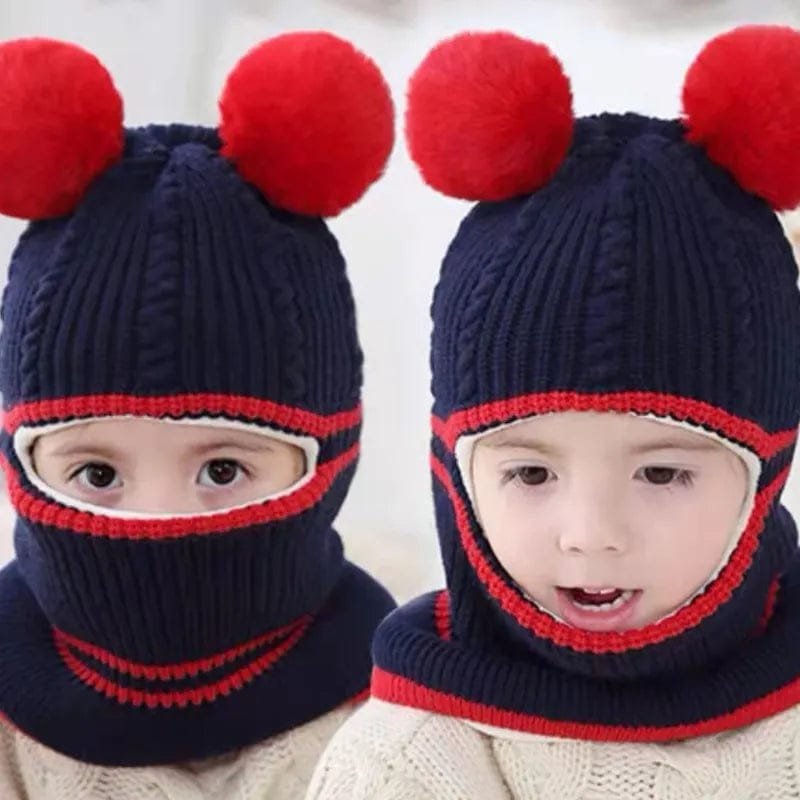 Two children wearing navy blue knit hats with red pom-poms on a light background