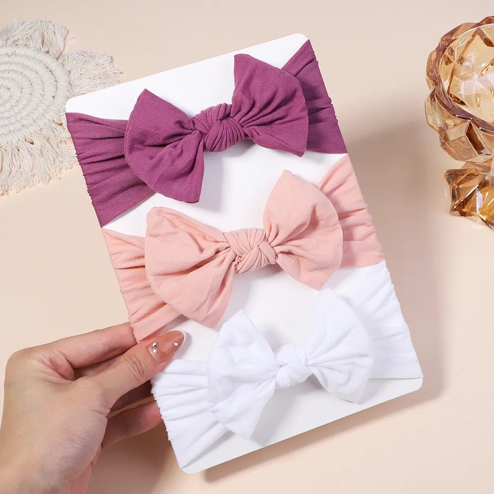 Three headbands with large bows in purple, pink, and white.