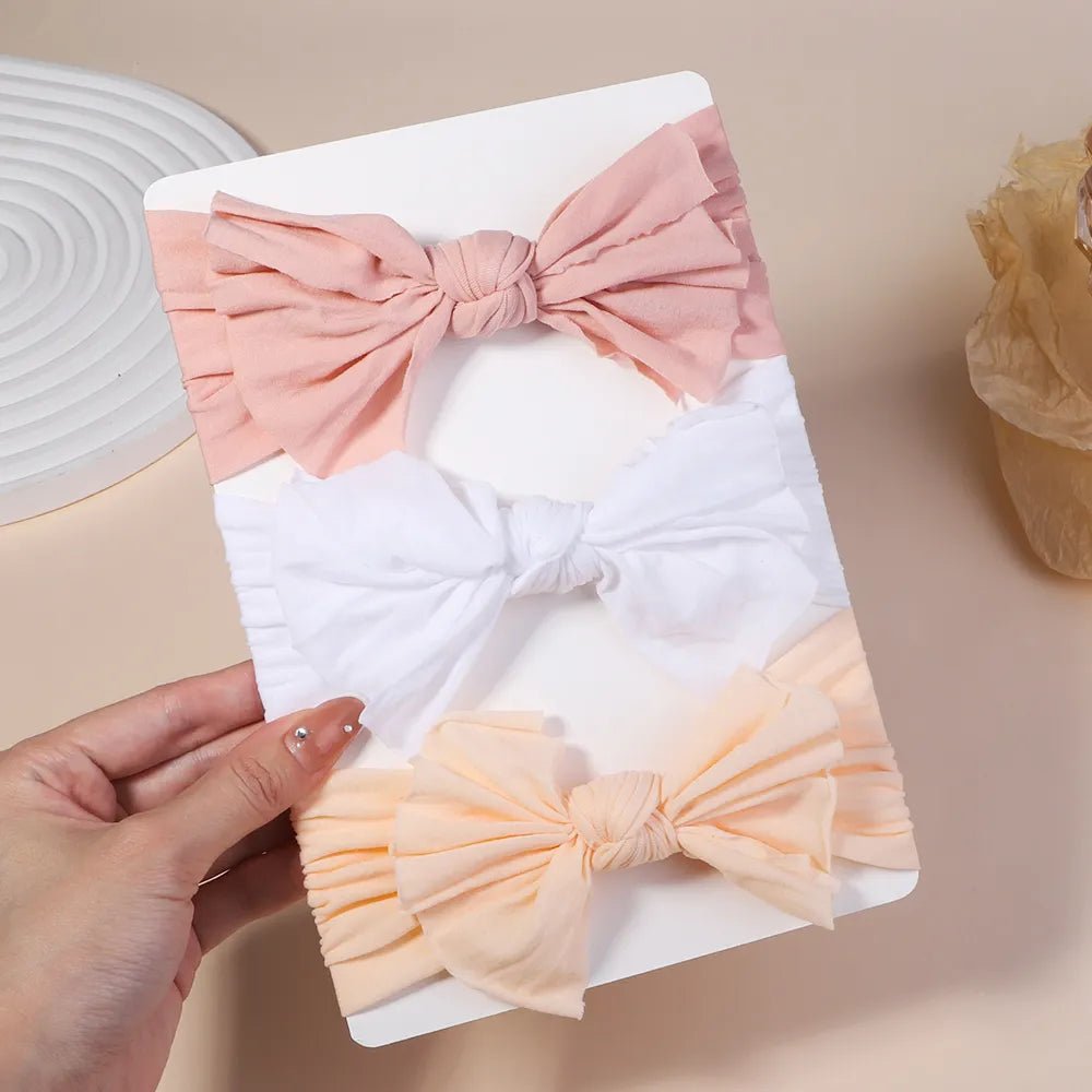 Set of bow-shaped hair accessories on a white card held by a hand against a beige background