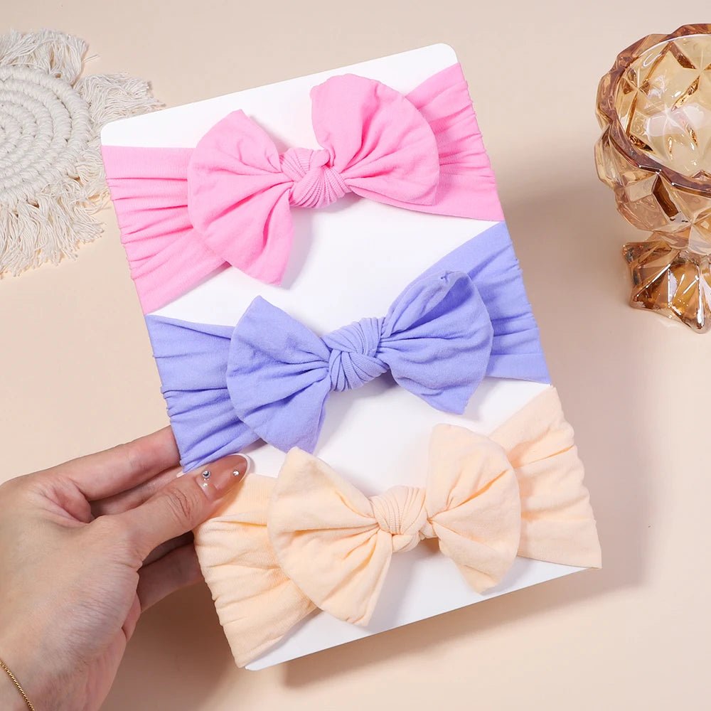Three colorful fabric bows held by a hand on a beige surface.