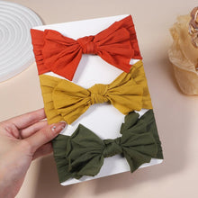 Three colorful hair bows on a white tray held by a hand against a beige background