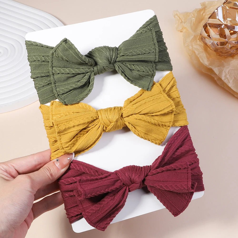 Three fabric bows in green, yellow, and red held by a hand on a white surface.