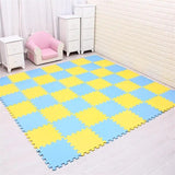 Checkered blue and yellow foam mat on a floor with white furniture and pink chair in the background.