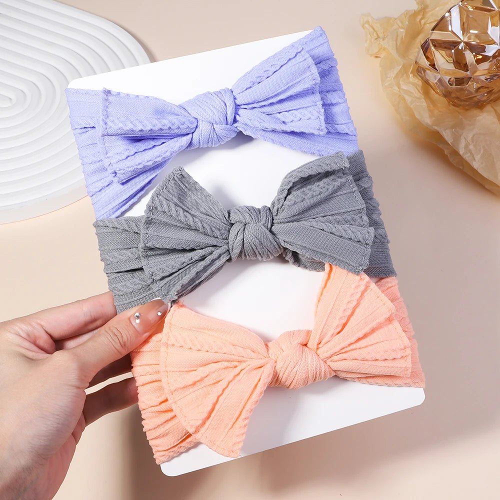 Three colorful bow-shaped hair accessories on a white box with a hand holding one of them.