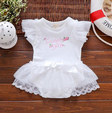 White baby dress with lace details and 'Sweet Angel' text on a wooden surface. (option 6)