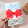 Three colorful hair bows on a white card held by a hand.
