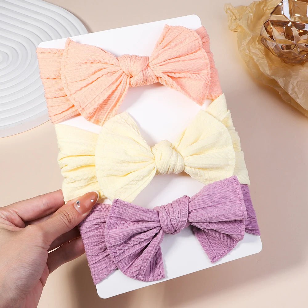 Three colorful bow hair accessories on a white tray with a hand holding one of them.