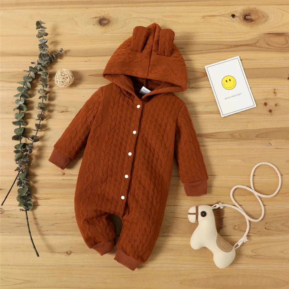 Brown baby romper with buttons on a wooden surface, next to a toy and decorative elements. (option 4)