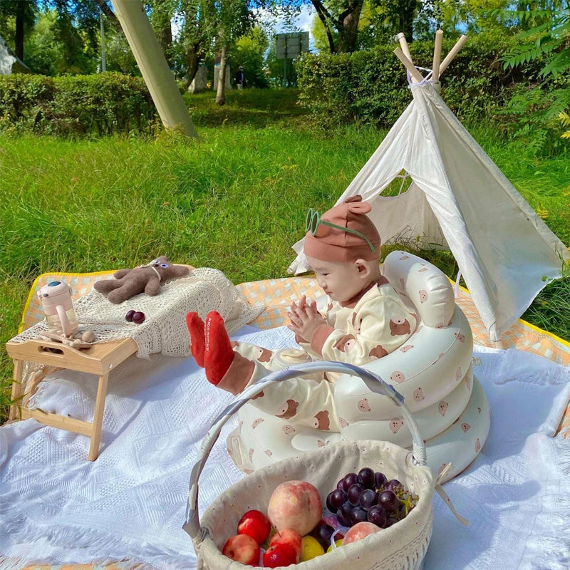 Baby sitting in an inflatable playpen sofa outdoors near a tepee for backyard play and floor seating.