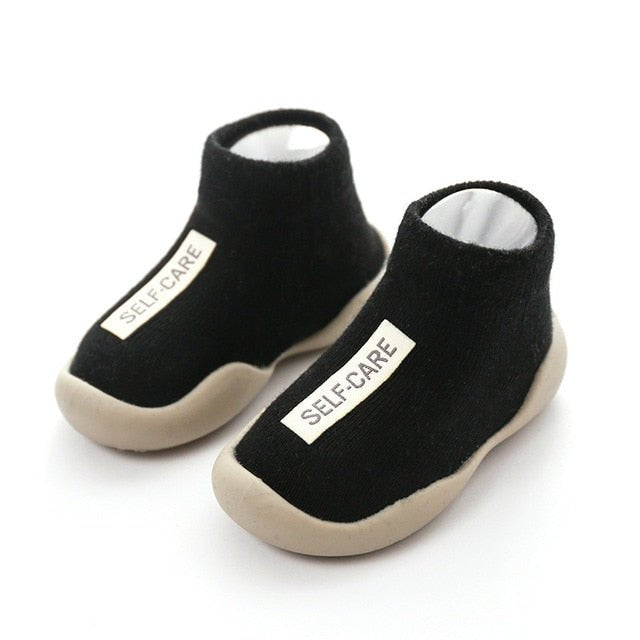 Black slip-on shoes with 'SELF-CARE' label on a white background