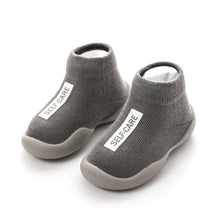 Gray children's shoes with 'SELF-CARE' label on a white background