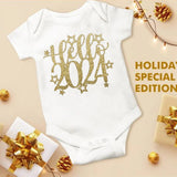 White baby onesie with gold 'Hello 2024' text, surrounded by holiday decorations