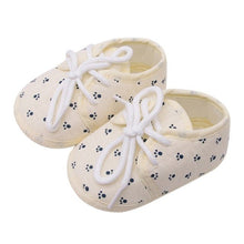 Pair of cream-colored baby shoes with black paw prints and white laces 