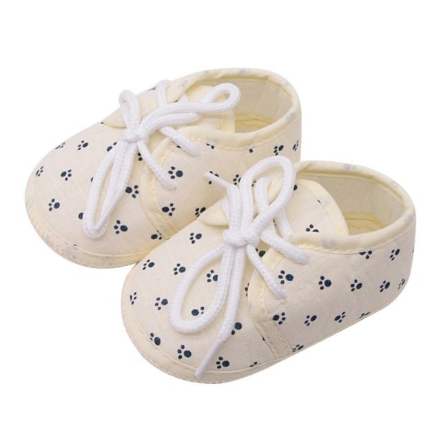 Pair of cream-colored baby shoes with black paw prints and white laces 