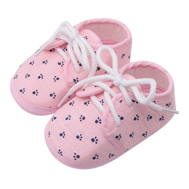 Pink baby shoes with white laces and paw print pattern 