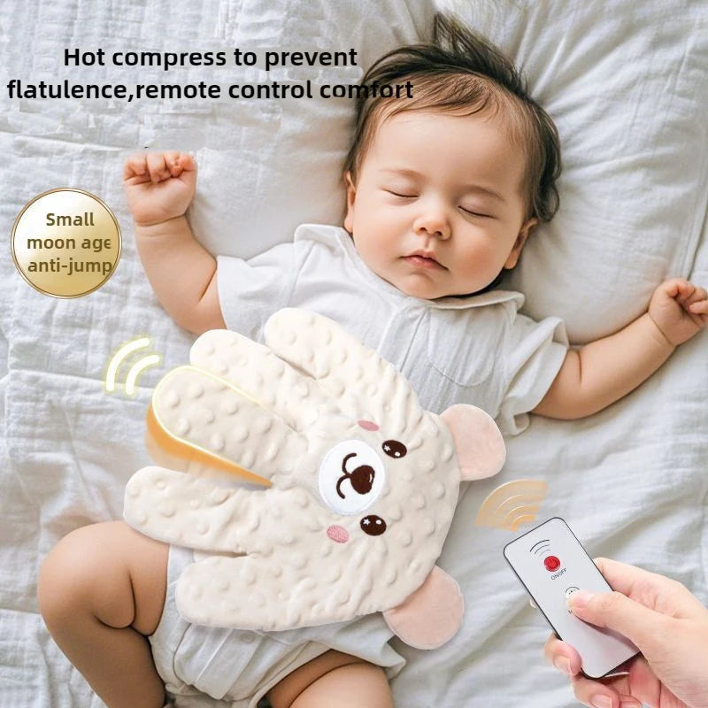 Baby lying down with a cream bear-face palm pillow on the tummy and a hand holding a remote control