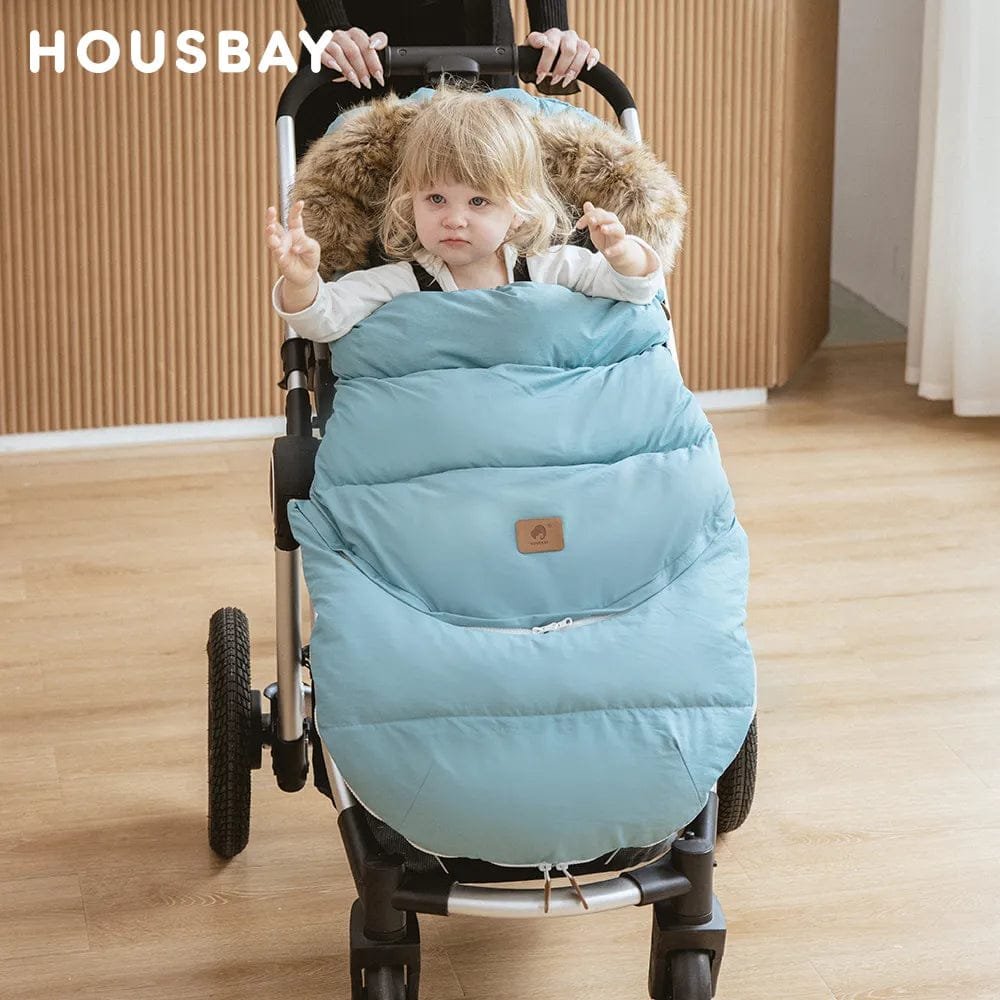 Child seated in a stroller wrapped in the blue winter footmuff, keeping infants insulated during cold-weather outings.