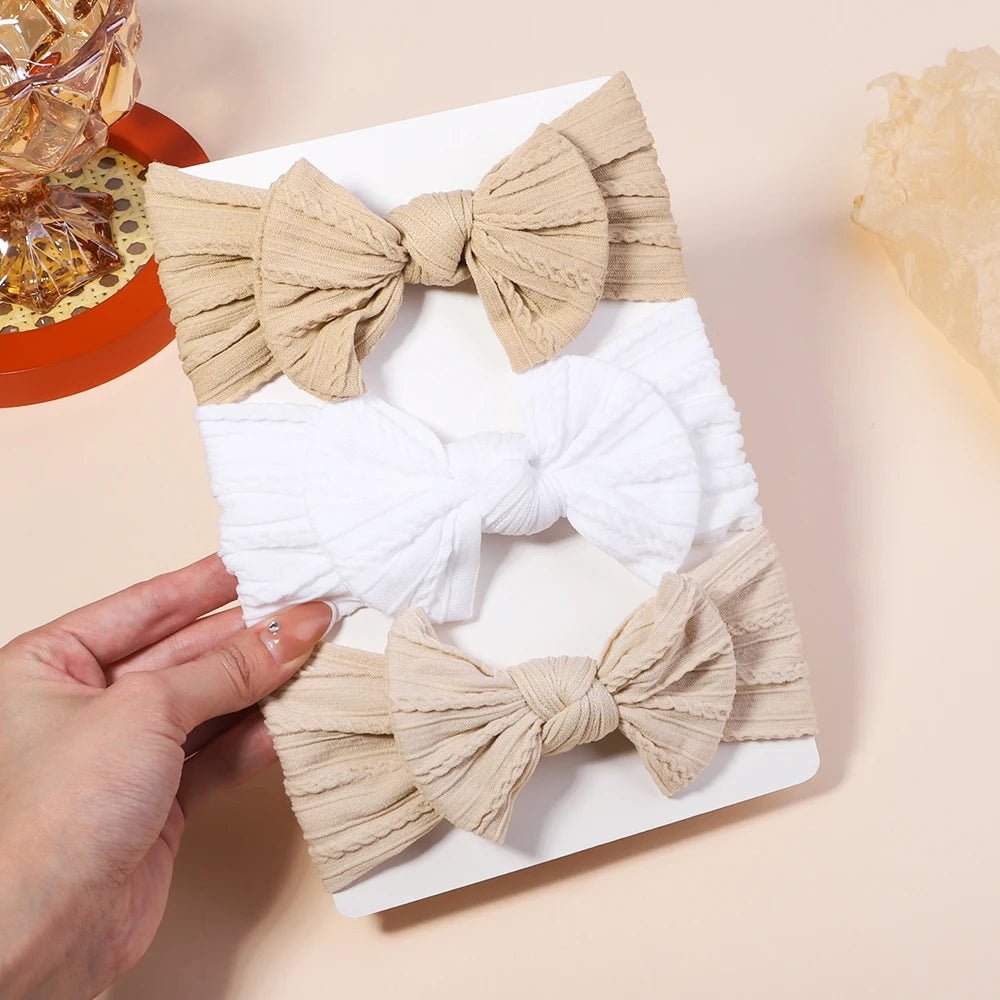 Two beige bows on a white card with a hand holding it.